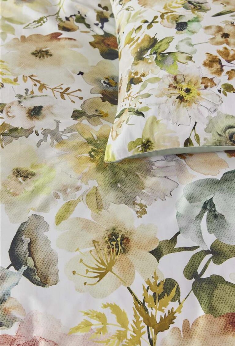 Nahaufnahme eines Bettes mit Kissen und Bettwäsche von Bettwäsche Beddinghouse Aquitaine, die einen botanischen Blumendruck in sanften Grün-, Gelb- und Beigetönen für einen sanften, natürlichen Look zeigt.