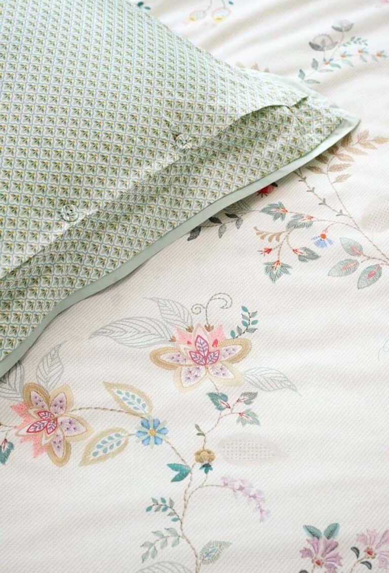 Eine Nahaufnahme von Bettwäsche Pip Studio Kili Flower: ein grün gemusterter Kissenbezug gepaart mit einem weißen Bettlaken, beide mit zarten pastellfarbenen Blumenmustern verziert.