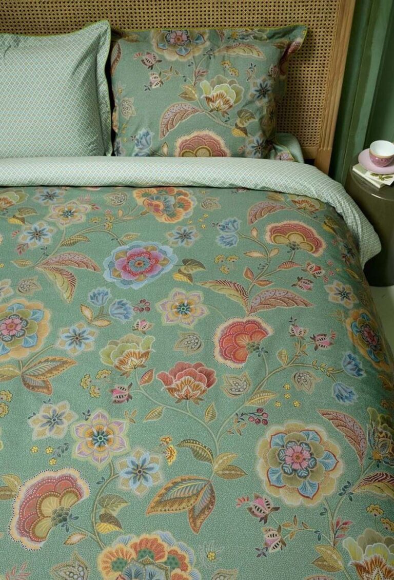 Die Bettwäsche Pip Studio Matata mit einem leuchtend grünen Blumenmuster und einem passenden Kissen mit bunten Blumen schmückt das Bett neben einem Nachttisch mit Tasse und Untertasse.