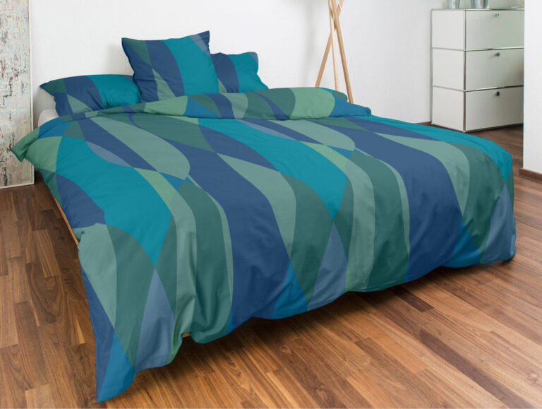 Auf einem ordentlich gemachten Bett liegt die Bettwäsche Nobilium Happening in teal, blau und grün gestreift, mit passenden Kissen. Das Zimmer verfügt über eine weiße Kommode, eine moderne Stehlampe, einen Holzboden und eine weiße Wand im Hintergrund.