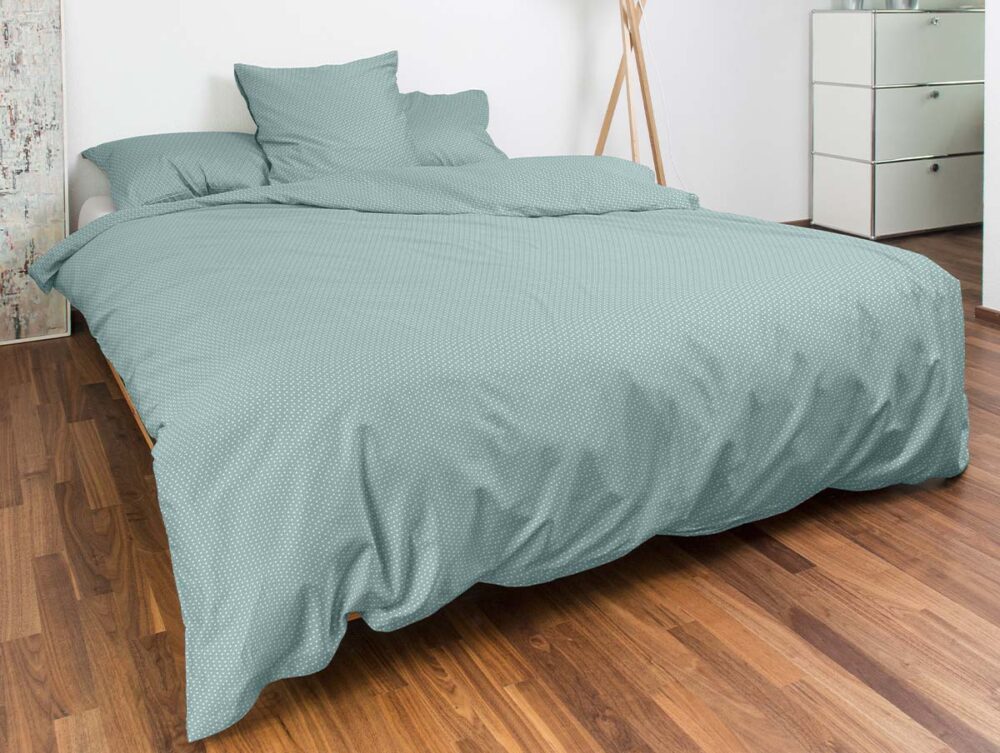 Ein modernes Schlafzimmer mit Holzböden und minimalem Dekor verfügt über ein ordentlich gemachtes Bett, das mit hellgrünem Bettwäsche Night Fashion Käthi und passenden Kissen bezogen ist, sowie eine schlichte weiße Kommode.