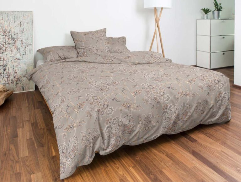 Ein modernes Schlafzimmer mit einem gemütlichen Bett aus Bettwäsche Nobilium Rufus mit beigen und grauen Mustern, ergänzt durch einen Holzboden, weiße Wände, eine Stehlampe, eine Kommode mit Pflanzen und abstrakte Kunst.