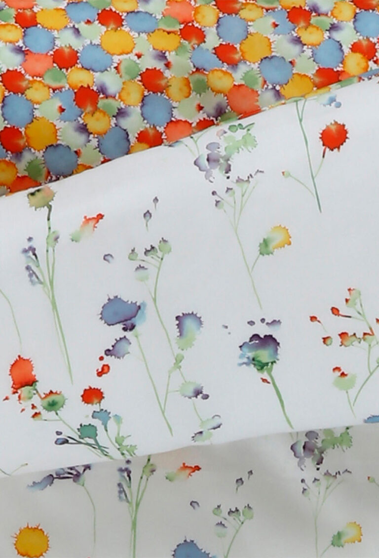 Zwei Stoffstücke: eines mit einem farbenfrohen, dichten Aquarell-Tupfenmuster - ideal für Bettwäsche Tamara-R Selection Silla& Shelly - und eines mit einem spärlichen floralen Aquarellmuster auf Weiß, die beide den charakteristischen Stil der Kollektion widerspiegeln.