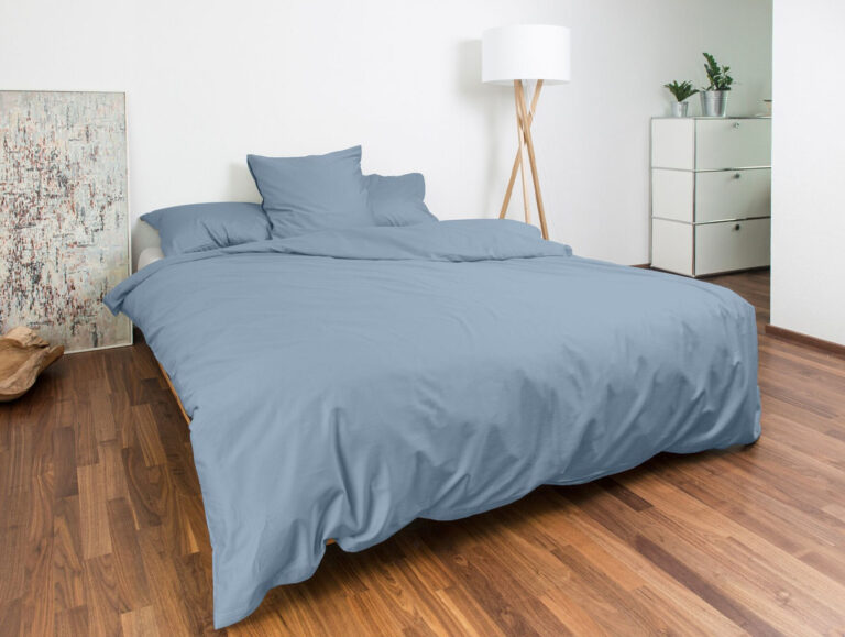 Minimalistisches Schlafzimmer mit einem ordentlich gemachten Bett mit hellblauer Bettdecke und Kissen, Holzboden, weißen Wänden, einer Stehlampe, einer Kommode mit Pflanzen und einem großen Gemälde an der Wand.