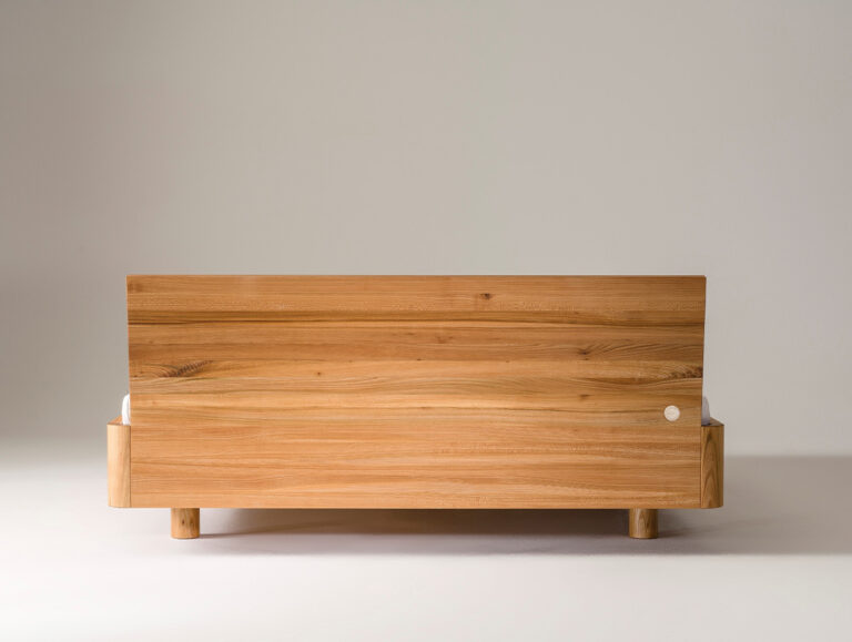 Ein moderner Bettrahmen aus Holz mit glattem, minimalistischem Design und einem breiten, rechteckigen Kopfteil, dargestellt vor einem schlichten, hellen Hintergrund.