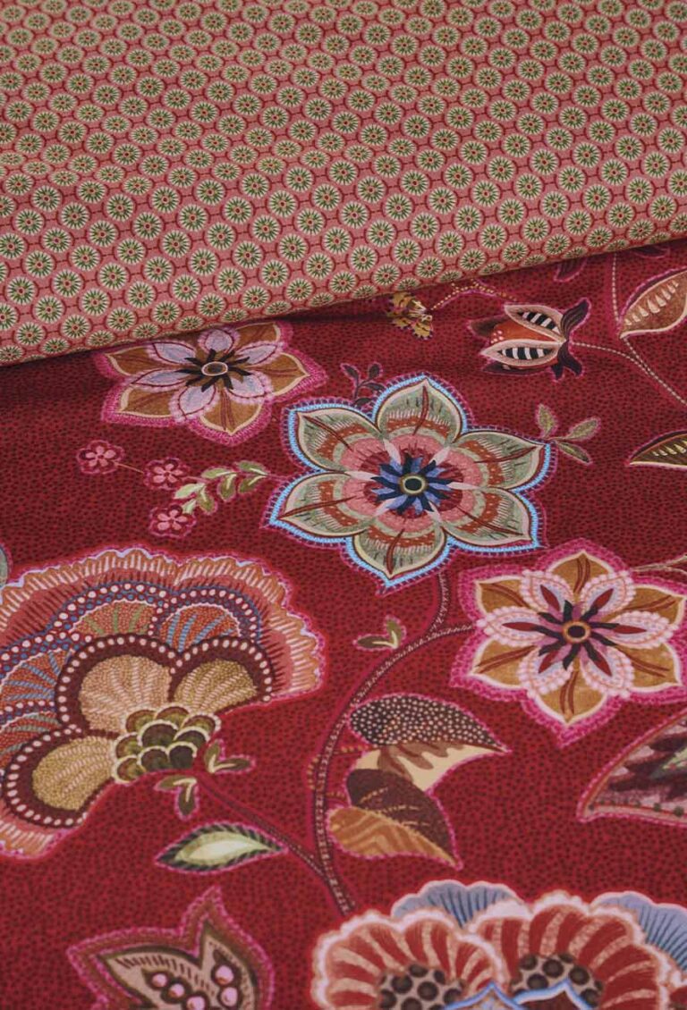 Zwei Stoffe: Das Oberteil hat ein kleines grünes und rotes geometrisches Muster, während das Unterteil, inspiriert von Bettwäsche Pip Studio Matata, kühne, bunte Blumen auf einem tiefroten Hintergrund zeigt.
