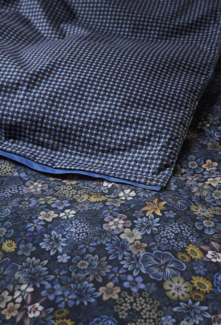 Eine Nahaufnahme von Bettwäsche Pip Studio Tutti i Fiori zeigt ein Kissen mit einem blau-weißen geometrischen Muster auf einem Laken mit einem dunkelblauen Blumenmuster.
