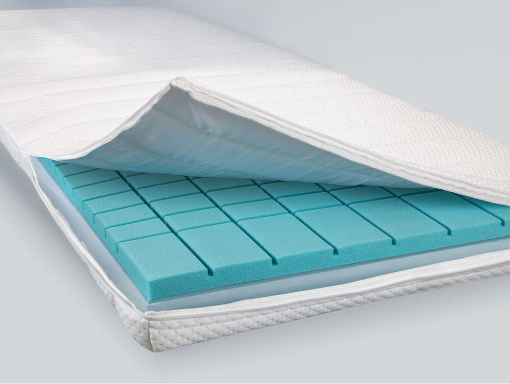 Eine Nahaufnahme einer Matratze aus dem Hasena Boxspringbett Classic "James Fiona" zeigt den weißen Steppbezug, der teilweise geöffnet wurde und blauen, in Rechtecke unterteilten Schaumstoff zum Vorschein bringt. Der Hintergrund ist einfarbig und in hellen Farben gehalten.