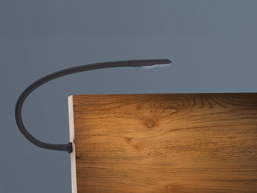Eine biegsame schwarze Leselampe ist an der Kante einer Holzfläche vor einem schlichten grauen Hintergrund befestigt. Der Hals der Lampe ist gebogen und ihr Licht ist ausgeschaltet.