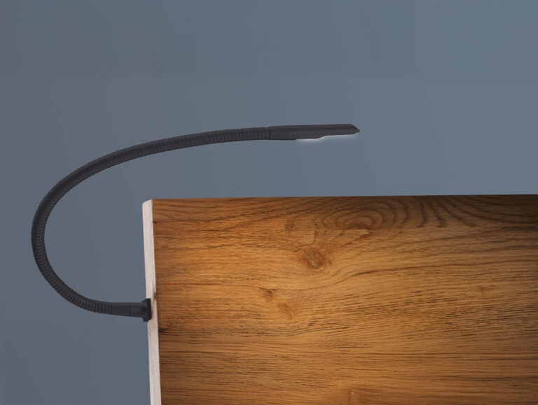 Eine biegsame schwarze Leselampe ist an der Kante einer Holzfläche vor einem schlichten grauen Hintergrund befestigt. Der Hals der Lampe ist gebogen und ihr Licht ist ausgeschaltet.