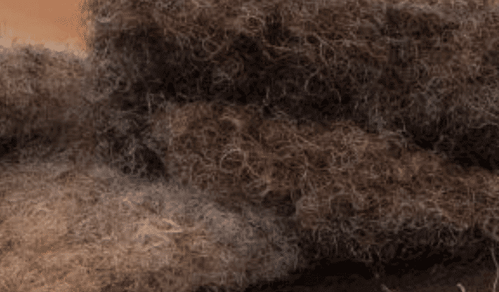 Nahaufnahme von groben, bräunlich-grauen Fasern mit einer rauen und verworrenen Textur, die an unverarbeitete Wolle oder natürliches Tierfell erinnern.