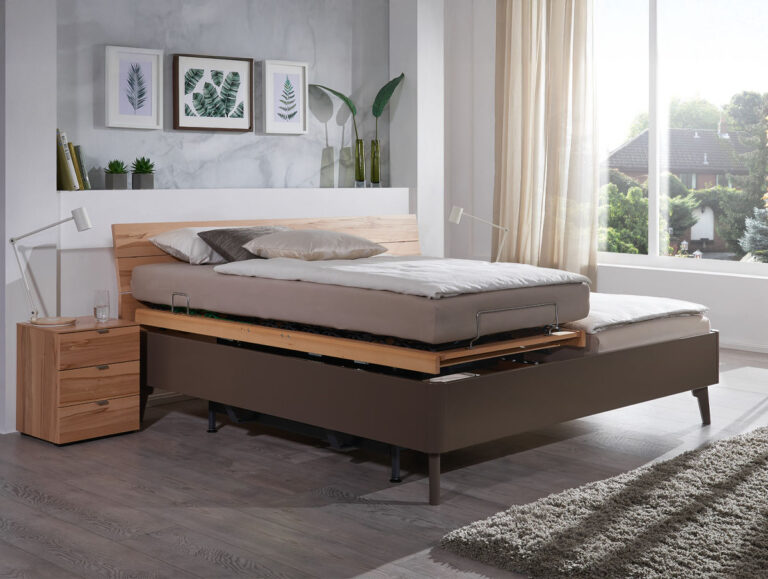 Ein modernes Schlafzimmer mit einem Holzbett mit verstellbarem Lattenrost, beiger Bettwäsche, zwei weißen Lampen, einem hölzernen Nachttisch, Wandkunst mit Blattdrucken und einem großen Fenster, das natürliches Licht hereinlässt.