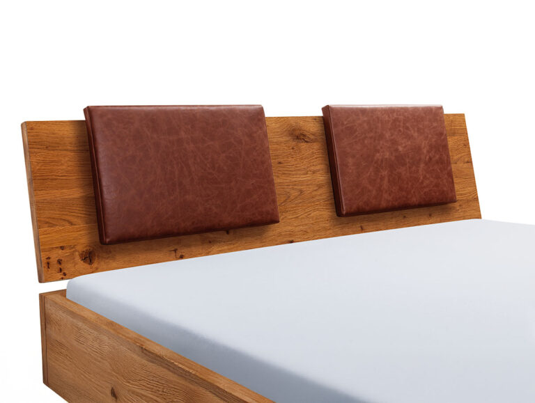 Ein hölzerner Bettrahmen mit einem Kopfteil mit zwei rechteckigen braunen Lederkissen und einer sauber gefertigten Matratze mit einem hellblauen Laken.
