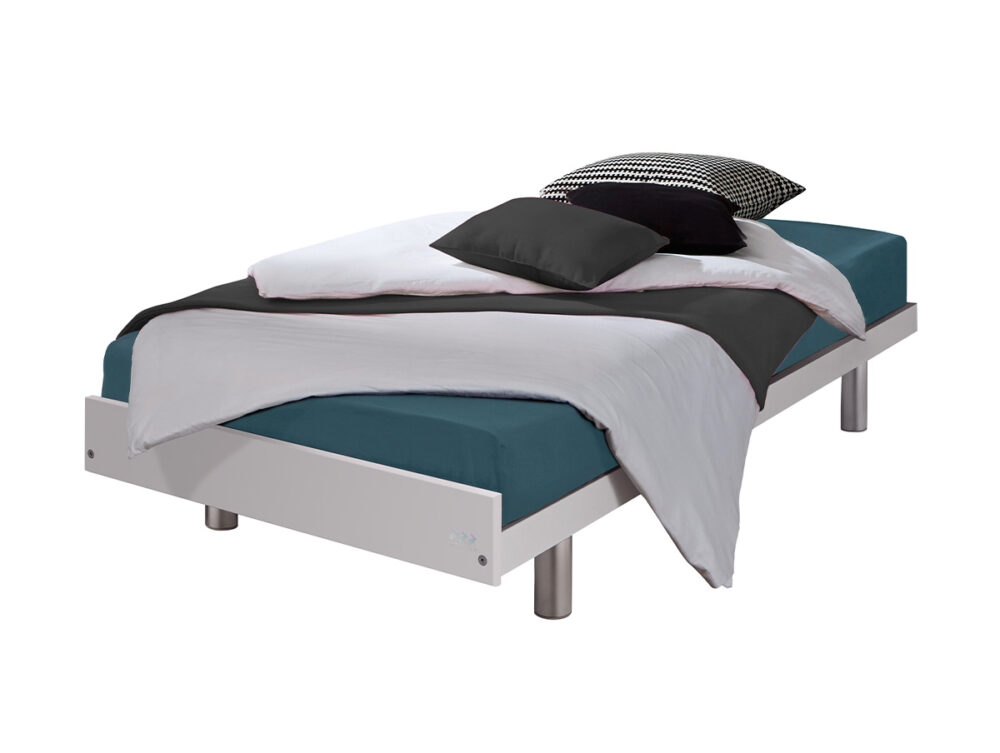 Das moderne Hasena "Econom" Couche Einzelbett hat einen weißen Rahmen mit Metallfüßen und ist mit einem blaugrünen Spannbettlaken, einer schwarz-weißen Bettdecke und drei Kissen - einem schwarzen, einem weißen und einem karierten - ausgestattet.