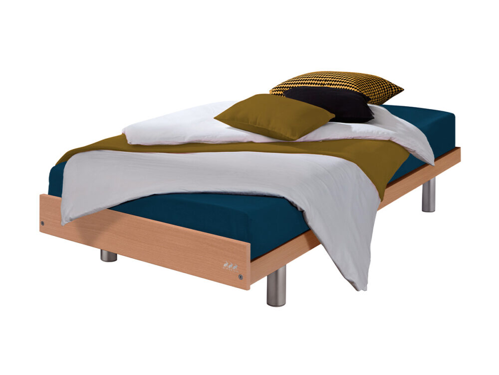 Die Hasena "Econom" Couche ist ein modernes Einzelbett mit einem hellen Holzrahmen, silbernen zylindrischen Beinen, einer blauen Matratze, weißem und olivgrünem Bettzeug und drei Kissen in Schwarz, Gelb und Olivgrün auf weißem Hintergrund.