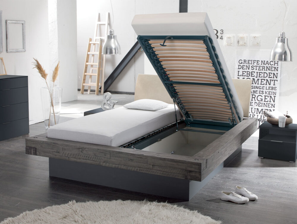 Ein modernes Schlafzimmer mit einer Hasena Bett "Factory-Line Bloc Practico-Box", einem hölzernen Stauraum-Bettgestell mit hochklappbarer Matratze, minimalistischem Dekor, Kommode, Leiterregal und zwei silbernen Pendelleuchten.
