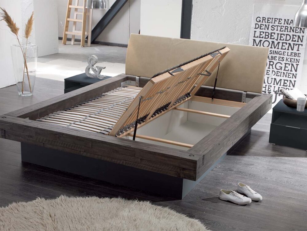 Die Hasena Bett "Factory-Line Bloc Practico-Box" bietet unter dem Lattenrost einen offenen Stauraum zum Hochklappen. Hier in einem schicken Schlafzimmer mit dunklem Boden, einem runden beigen Teppich und weißen Turnschuhen in der Nähe.