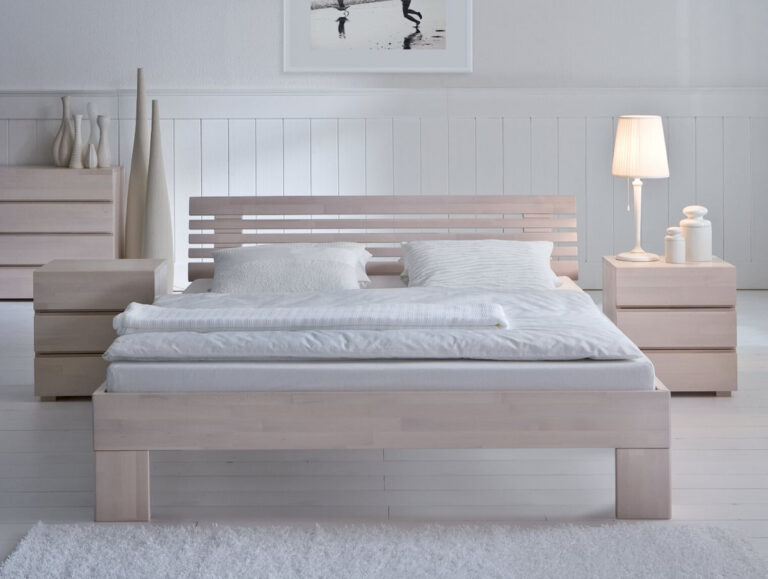 Ein minimalistisches Schlafzimmer mit dem Hasena Bett "Wood-Line Classic Massa" Holzbettgestell mit weißer Bettwäsche, zwei Nachttischen, einer Lampe, Vasen, einer Kommode und monochromer Wandkunst für einen klaren, hellen und modernen Look mit hellem Dekor.