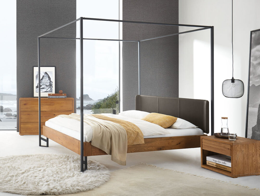 Ein modernes Schlafzimmer mit einem Himmelbett aus Holz, weißer und beiger Bettwäsche, einem runden Teppich, einem Nachttisch und einer Kommode aus Holz sowie einem großen Fenster mit Blick auf die Küste. Minimalistisches Dekor mit neutralen Tönen.