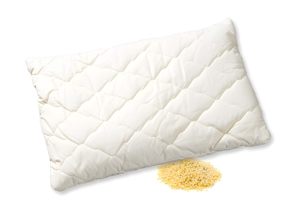 Das Hirsekissen "Hirsana" mit weißem Steppbezug ruht auf einer Fläche, unter der gelbe Hirsespelzen hervorlugen.