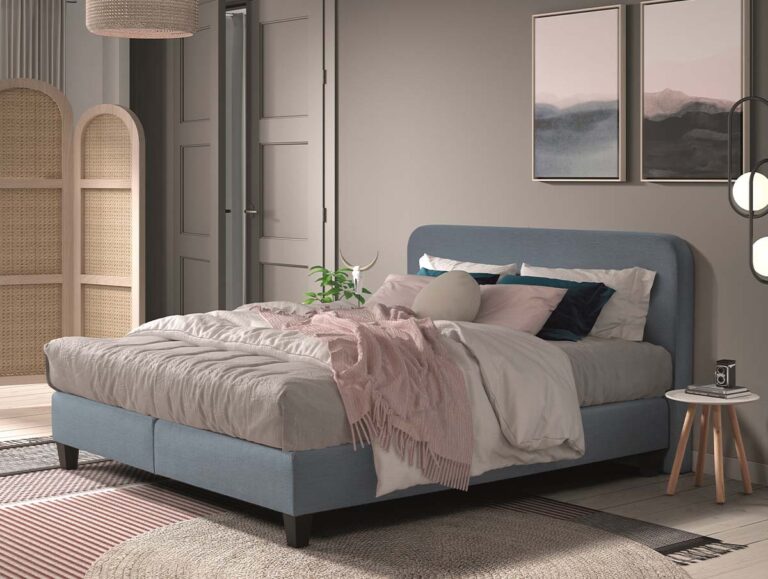 Ein gemütliches Schlafzimmer mit einem hellblauen Polsterbett, das mit weißer und rosa Bettwäsche ausgelegt ist. An der Wand befinden sich gerahmte abstrakte Kunstwerke, ein kleiner runder Beistelltisch mit einer Pflanze und eine warme, sanfte Beleuchtung.