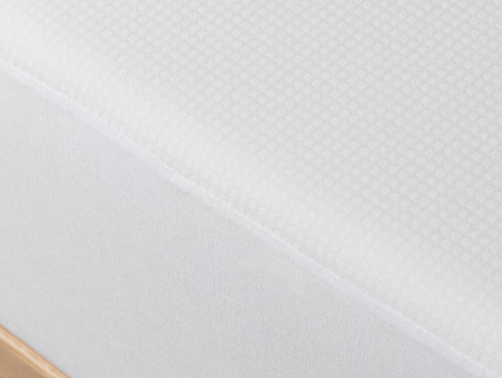Nahaufnahme der Velfont Fixleintuch Thermoregulierend Matratze mit weißem Bezug und dezentem Gittermuster auf einem Holzbettgestell.