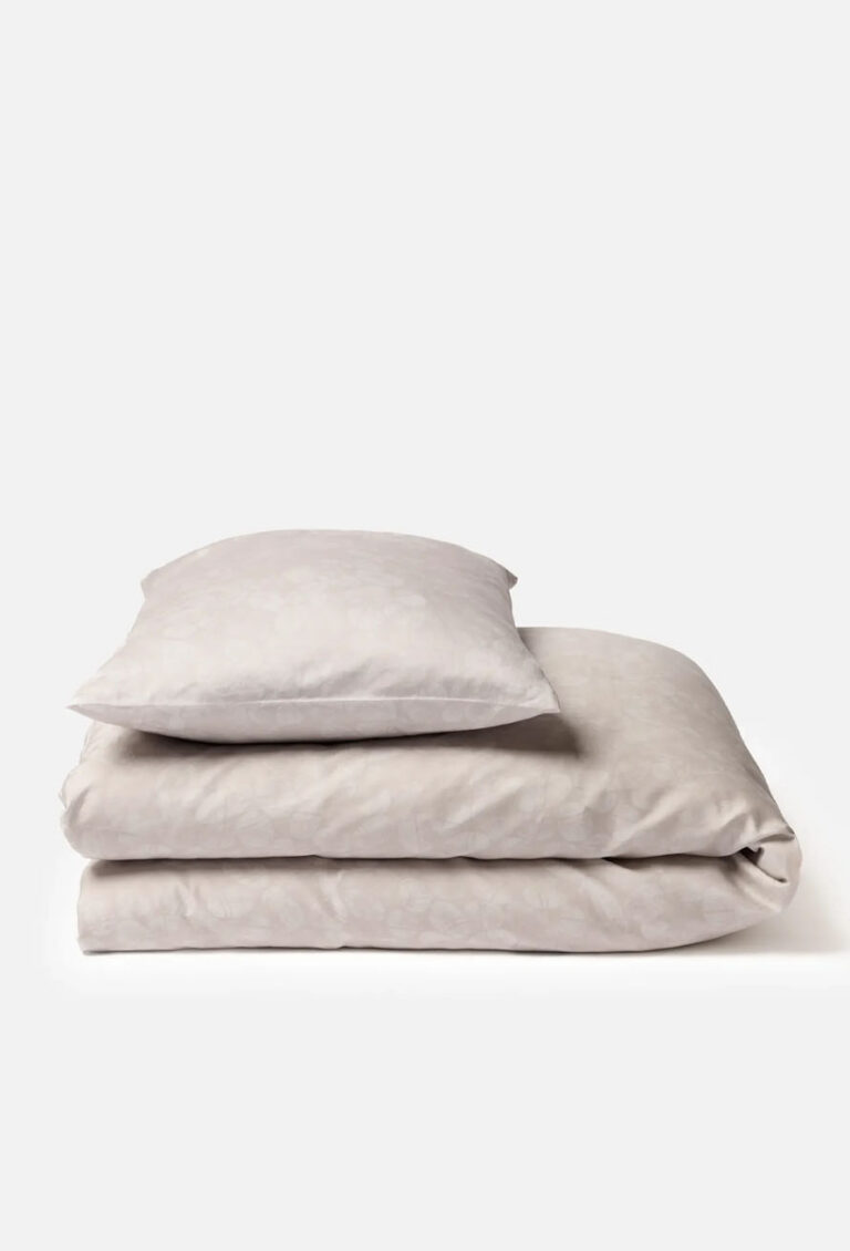 Ein ordentlich gefaltetes hellbeiges Bettwäscheset, einschließlich eines Kissens und einer Bettdecke, vor einem schlichten weißen Hintergrund.