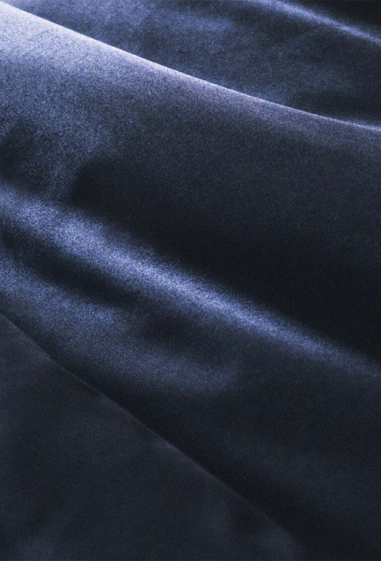 Nahaufnahme eines weichen, dunkelblauen Samtstoffs mit sanften Falten und einer glatten, leicht glänzenden Textur, die ein elegantes und luxuriöses Erscheinungsbild erzeugt.