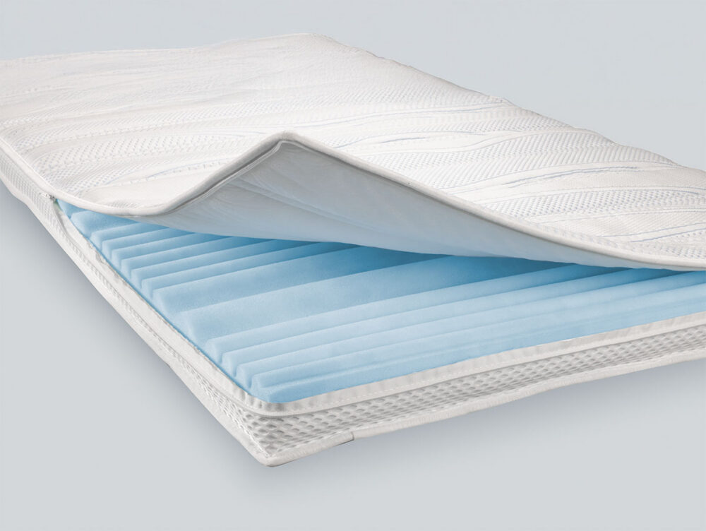 Nahaufnahme einer Matratze, bei der die oberste Schicht teilweise angehoben ist und eine hellblaue, strukturierte Schaumstoffschicht darunter zum Vorschein kommt, die den inneren Aufbau und die Materialien der Matratze veranschaulicht.