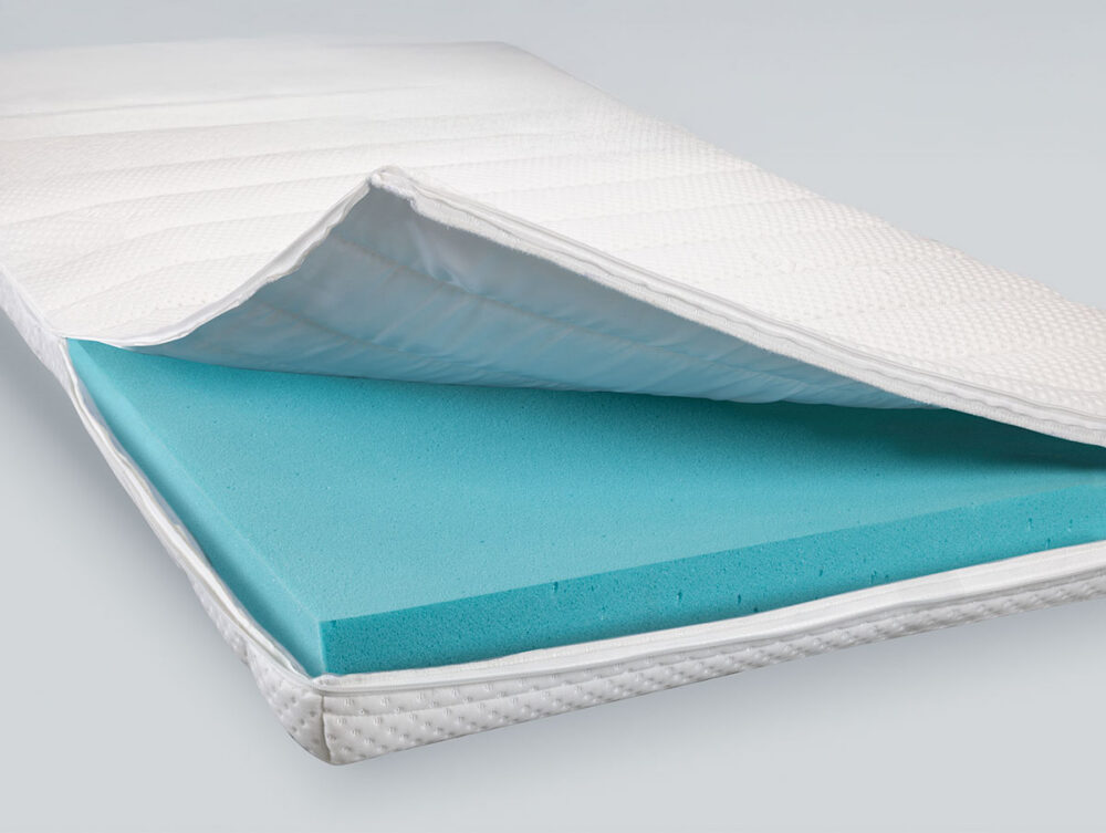 Eine Matratze mit einem weißen Steppbezug, der teilweise geöffnet wurde und eine Schicht blauen Schaumstoffs im Inneren offenbart. Der Hintergrund ist einfarbig und hell.