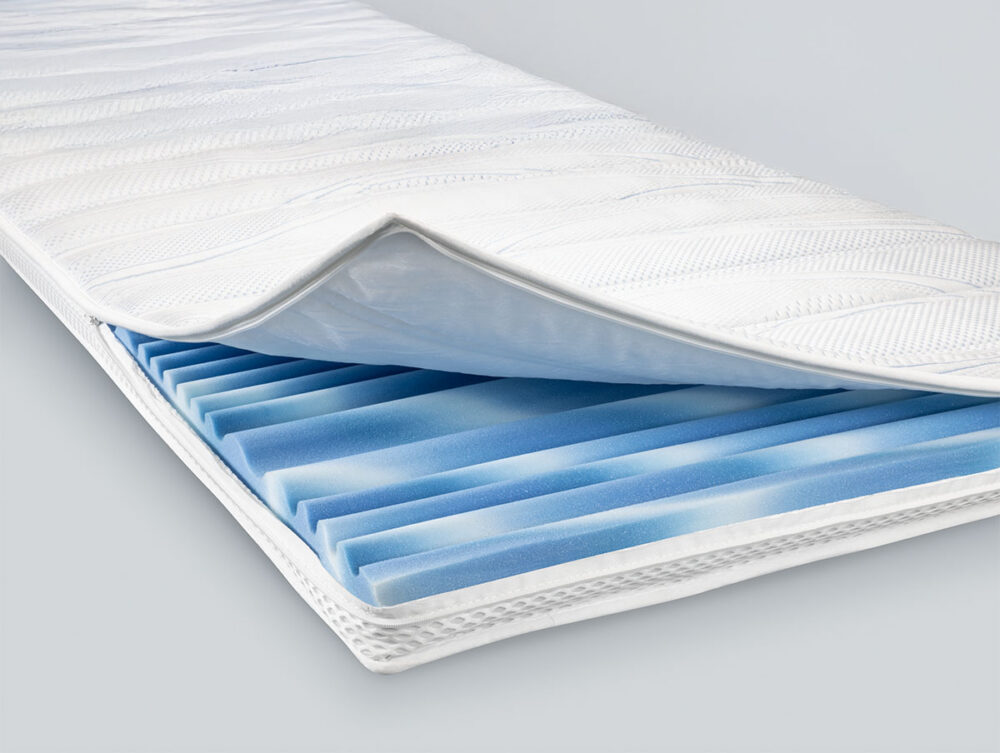 Eine Nahaufnahme einer Matratze mit weißem Bezug, der teilweise geöffnet wurde, zeigt blaue und weiße Memory-Schaumstoffschichten - eine ideale Kombination für zusätzlichen Komfort in Verbindung mit dem Hasena Topper "Marine-Top".