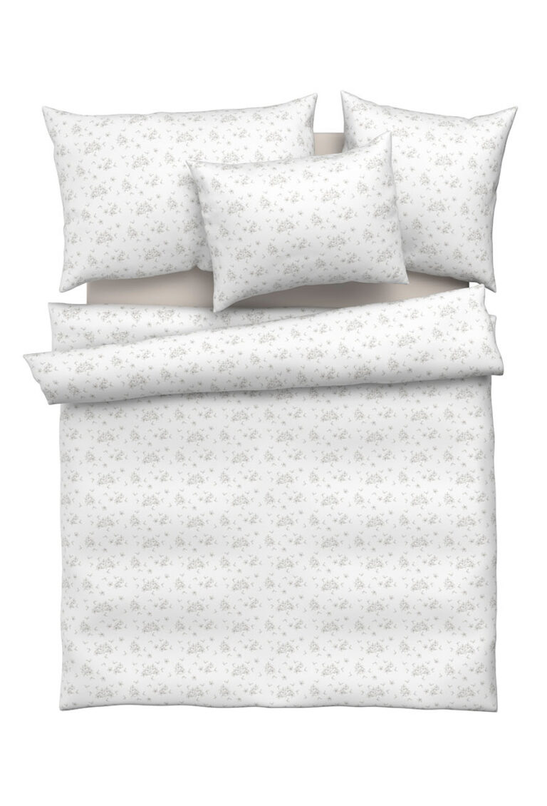 Ein ordentlich aufgebautes Bett mit weißer Bettwäsche, darunter zwei große Kissen, zwei kleinere Kissen und eine Bettdecke, die alle ein dezentes hellgraues Blumenmuster aufweisen.