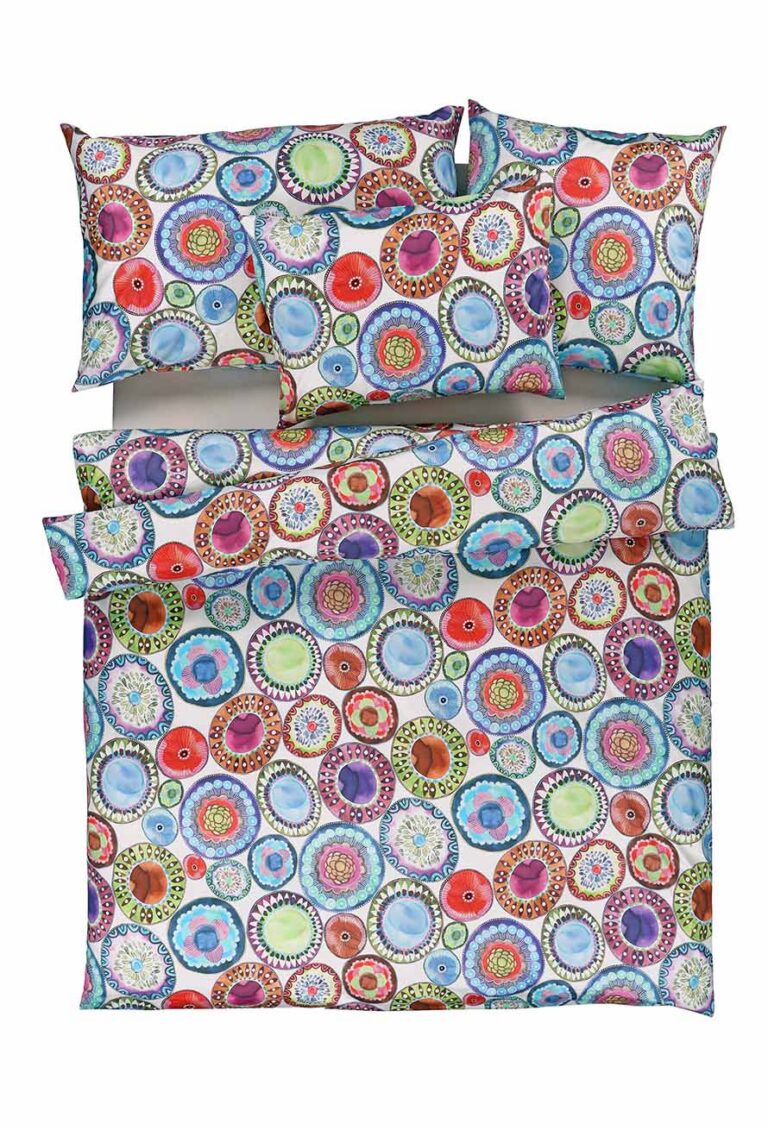 Ein Bett mit einem farbenfrohen Bettbezug und Kissen mit einem Muster aus sich überlappenden, bunten Kreisen und dekorativen Punkten auf weißem Hintergrund. Das Design ist lebendig und verspielt.