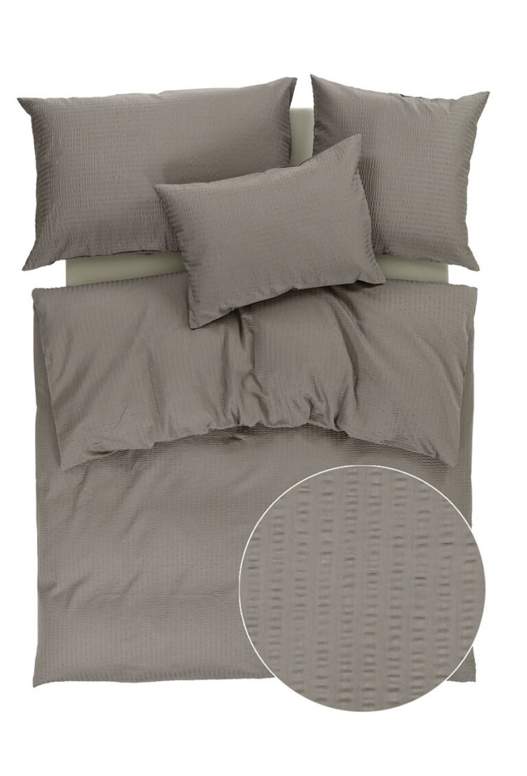 Ein sauber arrangiertes taupefarbenes Bettwäscheset mit drei Kissen und einem Bettbezug mit dezentem, strukturiertem Streifenmuster, das in einer Nahaufnahme mit kreisförmigem Einsatz gezeigt wird.