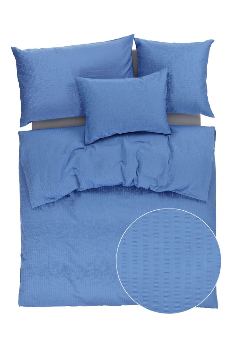 Blaue strukturierte Bettwäsche mit vier Kissen, einem Bettbezug und einer Nahaufnahme, die ein dezentes, quadratisch gemustertes Stoffmuster zeigt. Die Bettwäsche scheint ordentlich auf einem Bett angeordnet zu sein.