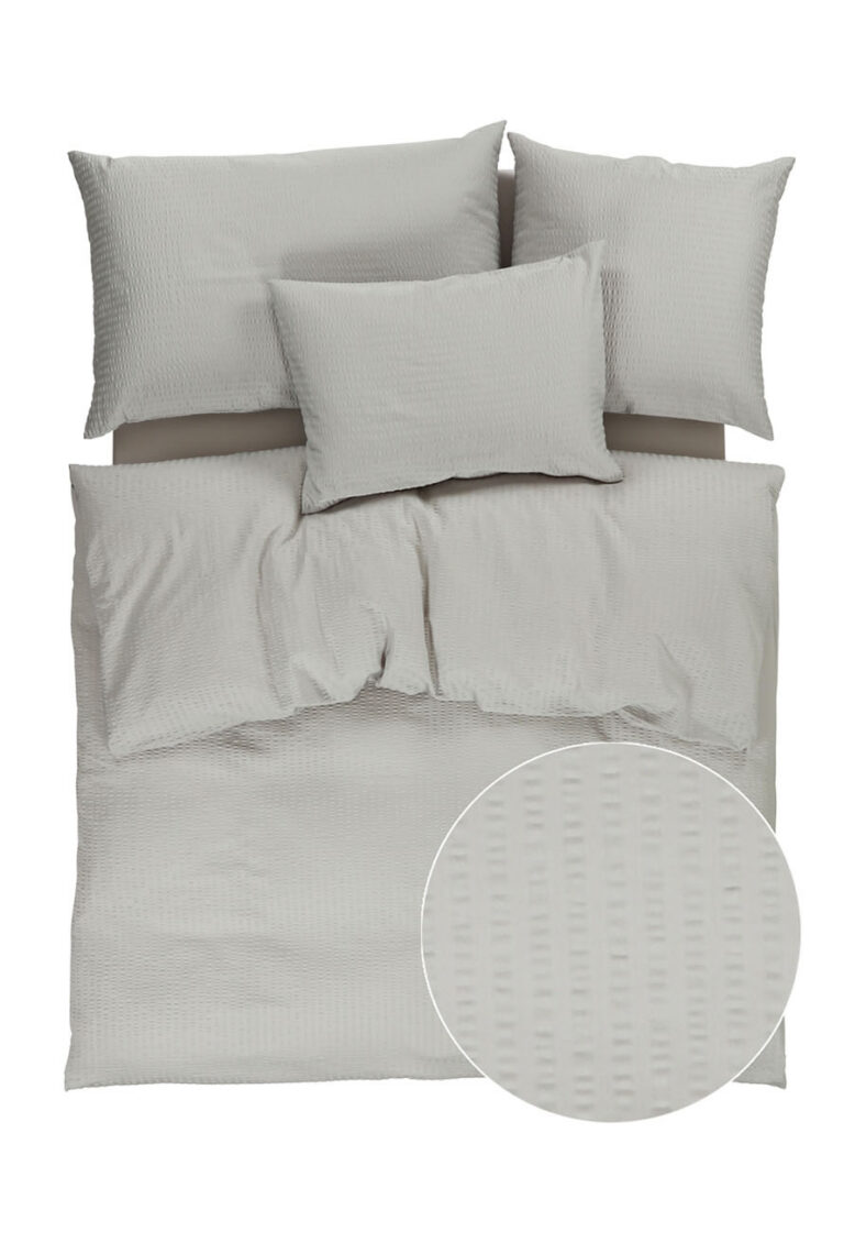 Ein ordentlich gemachtes Bett mit einem hellgrauen strukturierten Bettbezug und Kissenbezügen, von oben gezeigt. Ein eingesetzter Kreis hebt das subtile, rechteckige Webmuster des Stoffes hervor.