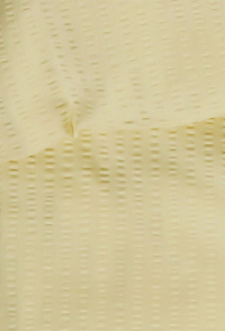 Nahaufnahme eines blassgelben, strukturierten Stoffes mit einem subtilen gitterartigen Muster und sanften Falten, die eine weiche und leicht erhabene Oberfläche bilden.