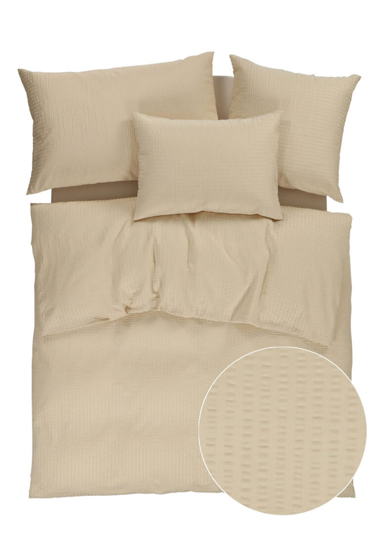 Ein beigefarbenes Bettwäscheset mit strukturiertem Muster, das einen Bettbezug und drei Kissen umfasst. Ein eingefügter Kreis zeigt eine Nahaufnahme der waffelartigen Struktur des Stoffes.