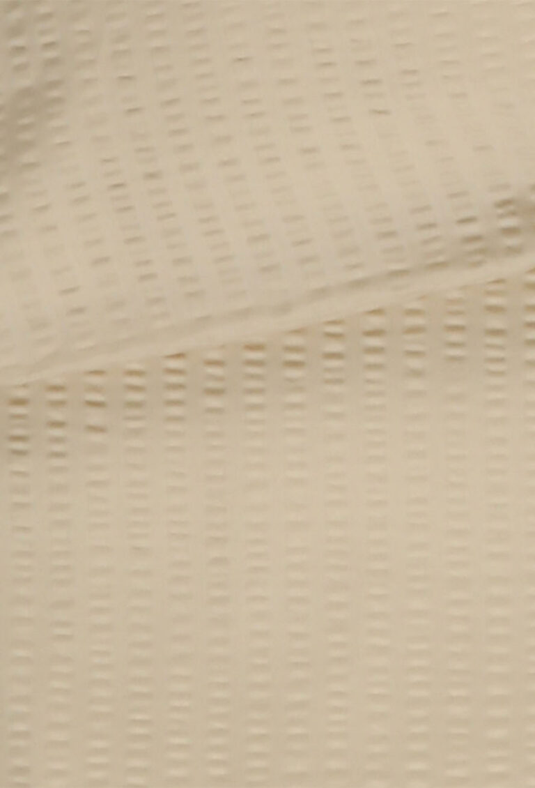 Nahaufnahme einer beigefarbenen strukturierten Oberfläche mit einem Muster aus kleinen, gleichmäßig verteilten rechteckigen Vertiefungen, die diagonal über das Material verlaufen.