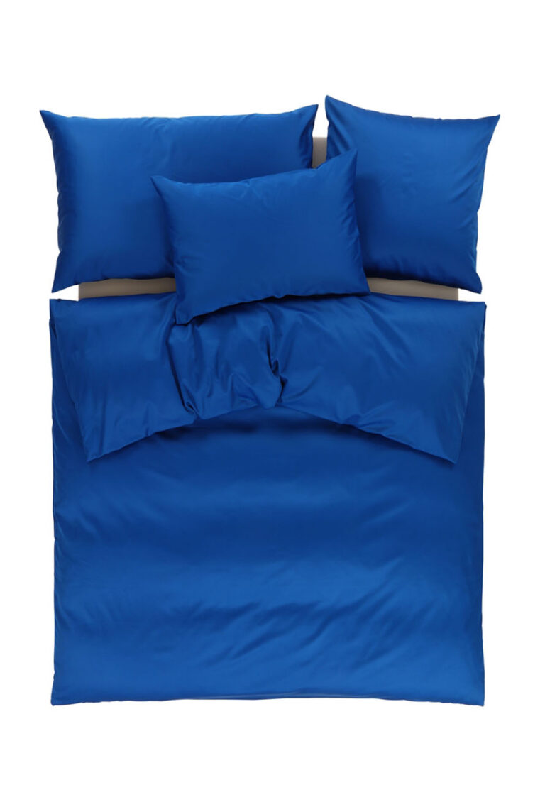 Draufsicht auf ein ordentlich gemachtes Bett mit vier Kissen und einer Bettdecke, alles in passender einfarbiger königsblauer Bettwäsche, vor einem weißen Hintergrund.