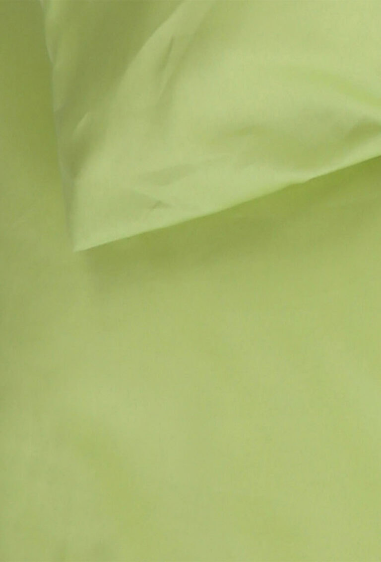 Eine Nahaufnahme eines hellgrünen Kissenbezugs und eines Bettlakens, wobei die weiche Stoffstruktur sichtbar ist und ein Teil des Kissens das Laken überlappt.