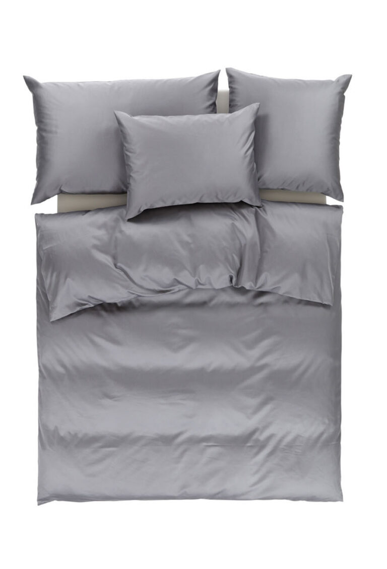 Ein ordentlich gemachtes Bett mit grauer Bettwäsche, darunter eine Bettdecke, zwei große und zwei kleinere Kissen, alles auf weißem Hintergrund.