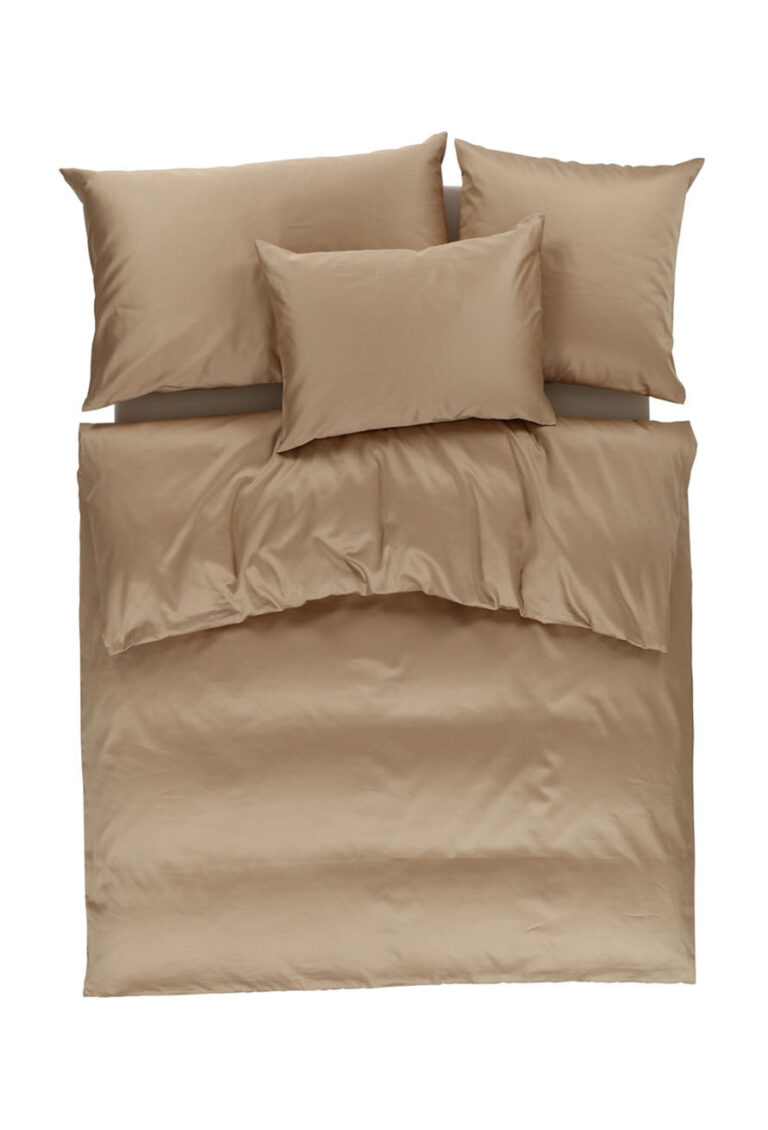 Ein ordentlich gemachtes Bett mit einem hellbraunen Bettbezug und drei passenden Kissen, fotografiert von oben vor einem weißen Hintergrund.