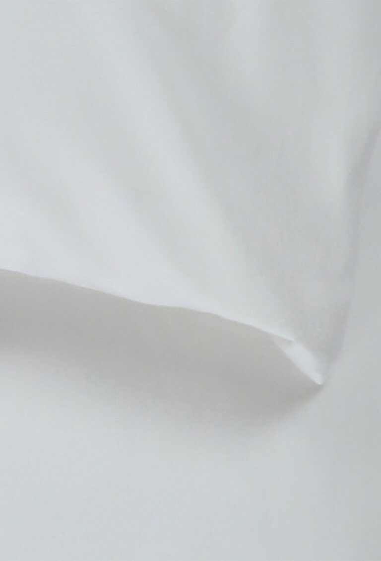 Nahaufnahme eines weißen Kissens, das auf einem weißen Bettlaken liegt. Man sieht eine Ecke des Kissens und einen Teil der Stoffoberfläche darunter.