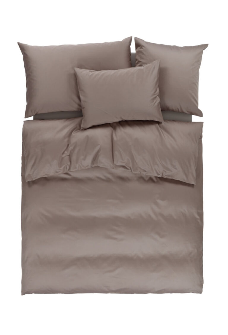 Ein ordentlich gemachtes Bett mit taupefarbenem Bettzeug, darunter zwei Kopfkissen, ein Kissen in der Mitte, ein Spannbetttuch und ein Bettbezug. Das Bettzeug erscheint glatt und weich, von oben fotografiert.