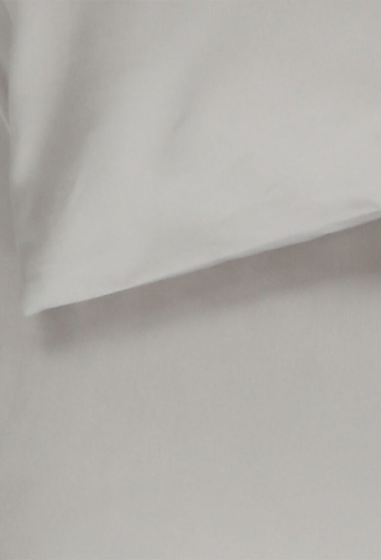 Eine Nahaufnahme eines weißen Kissens, das auf einem weißen Bettlaken liegt, zeigt einen glatten, sauberen Stoff bei sanfter Beleuchtung.