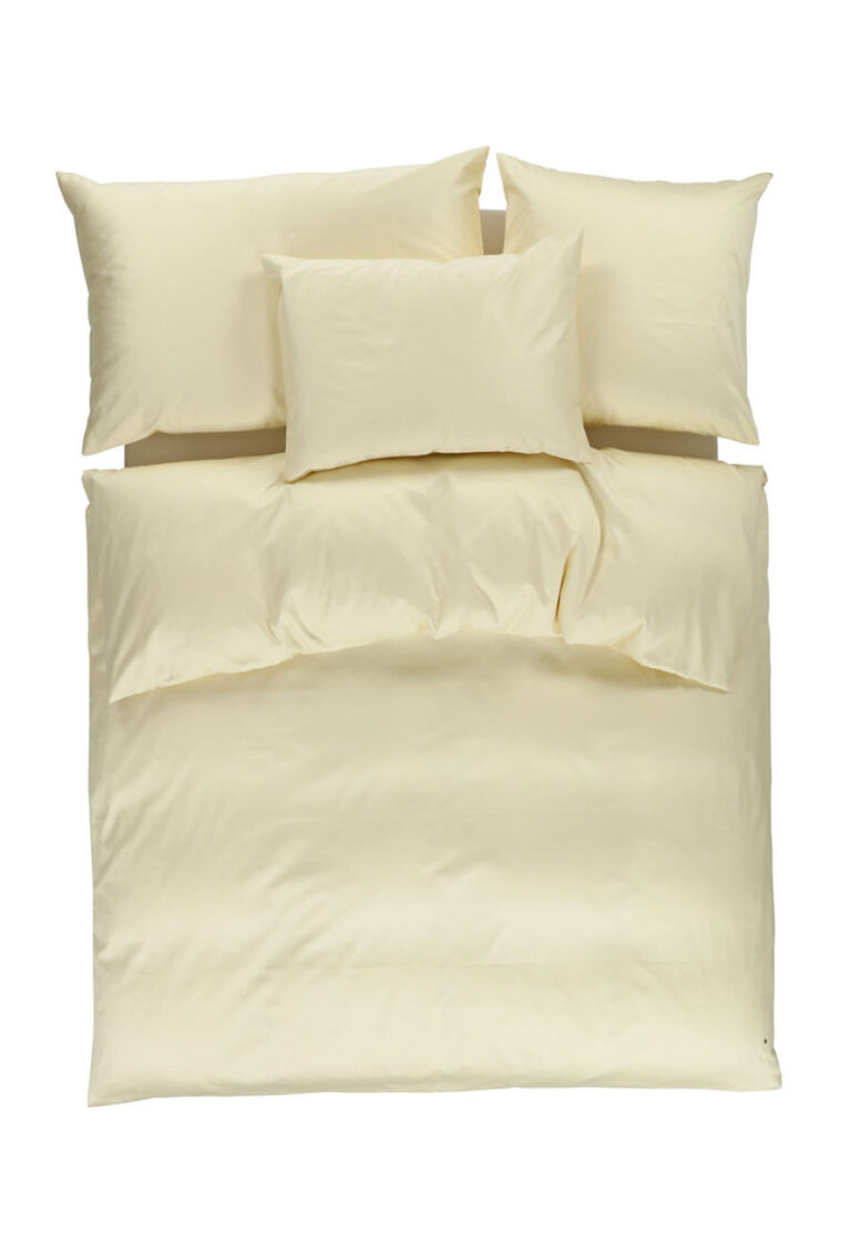 Ein ordentlich gemachtes Bett mit cremefarbener Bettwäsche, einschließlich eines Bettbezugs und drei Kissen, alles auf einem weißen Hintergrund von oben gesehen.