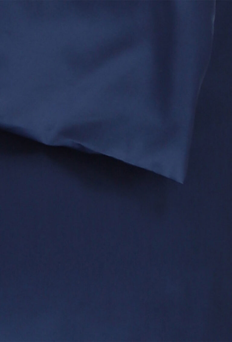 Eine Nahaufnahme eines glatten, dunkelblauen Stoffes mit einer markanten Falte, die eine sichtbare Naht und einen Schatten auf dem weichen Material erzeugt.