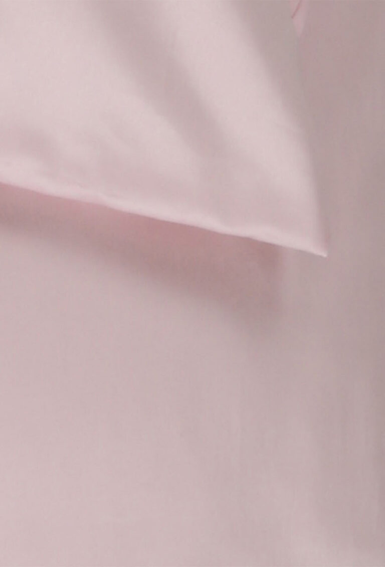 Eine Nahaufnahme eines weichen, hellrosa Kissens, das teilweise auf einem passenden rosa Laken oder einer rosa Oberfläche liegt.