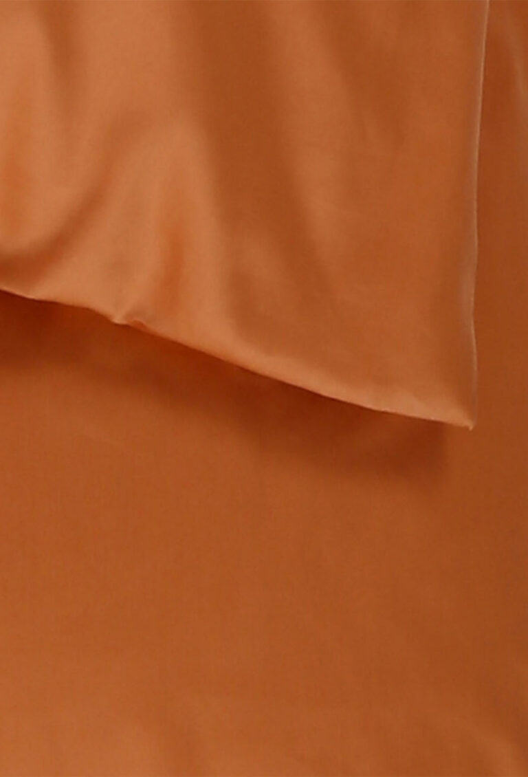 Eine Nahaufnahme eines glatten, rostfarbenen Stoffes mit leichtem Glanz, der sanfte Falten und weiche Schatten aufweist.